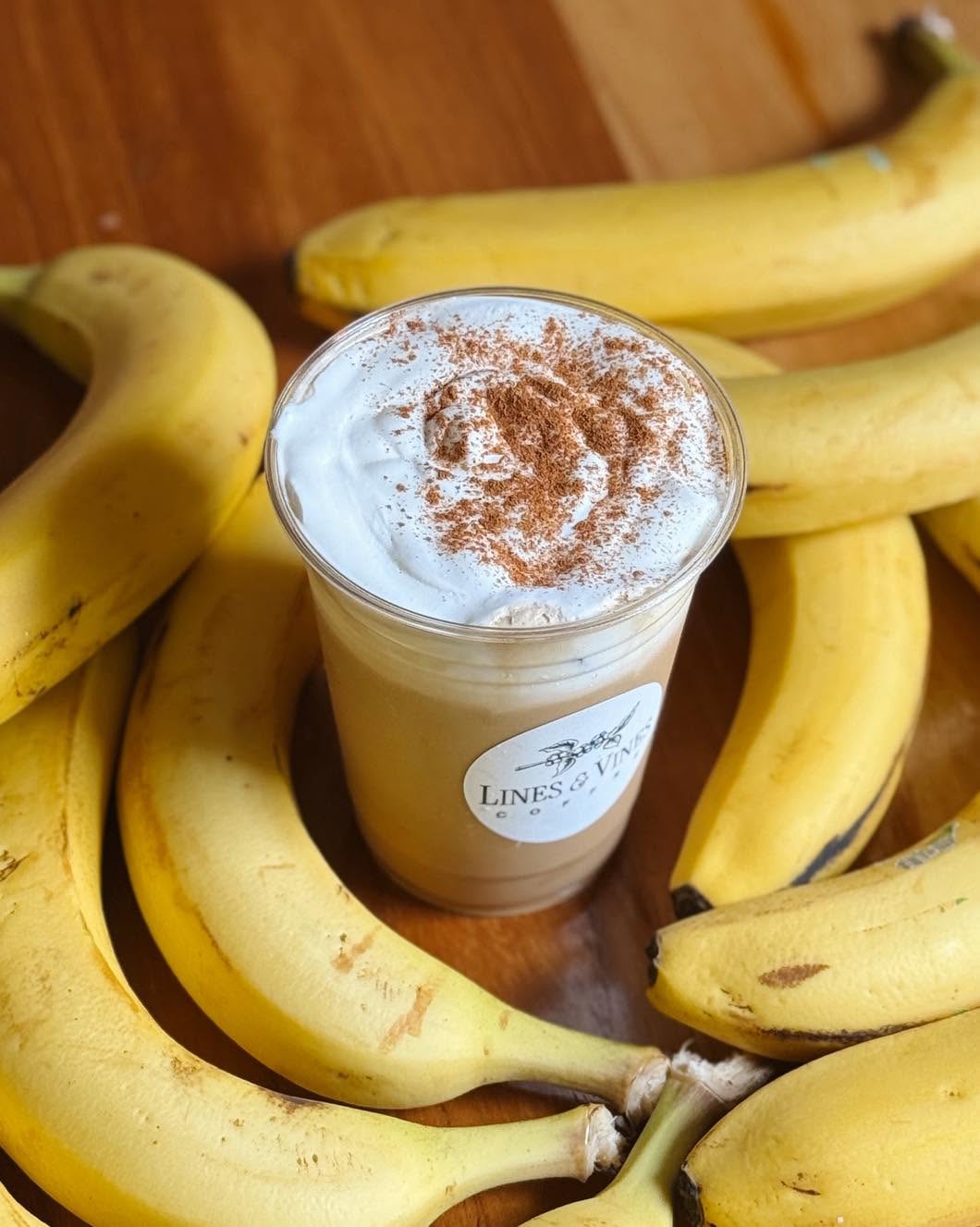 The signature Bananas Foster iced latte in a Lines & Vines cup, surrounded by fresh bananas