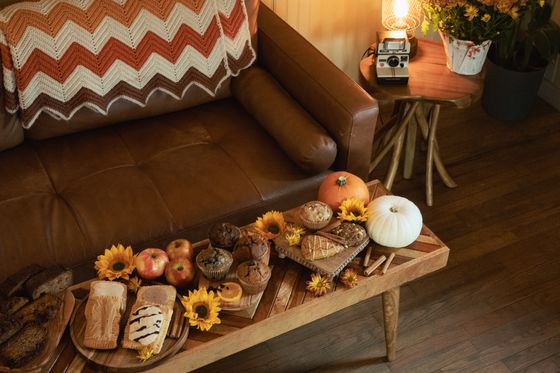 The fall bakery lineup laid out on a wooden bench in front of the shop's leather couch: loaf breads, muffins, a blondie, apples, pumpkins, and sunflowers
