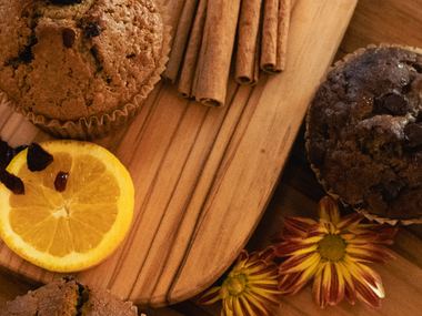 Muffins on a wooden board with a dried orange slice, cinnamon sticks, and autumn flowers