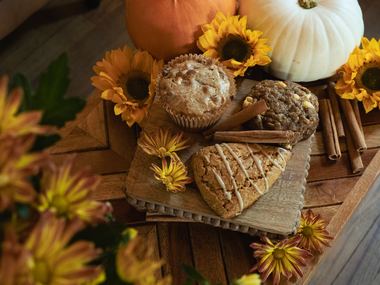 A pumpkin scone with icing drizzle, a Biscoff blondie, and a pumpkin white chocolate chip cookie, with pumpkins and sunflowers behind