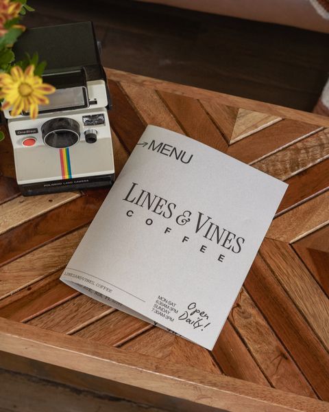 The shop's printed menu card, folded on a chevron wood table beside a Polaroid camera and yellow flowers