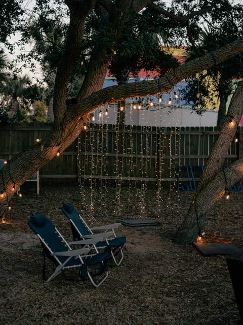 Lawn chairs under an oak tree hung with cafe lights and a curtain of fairy lights, set up for an outdoor movie night