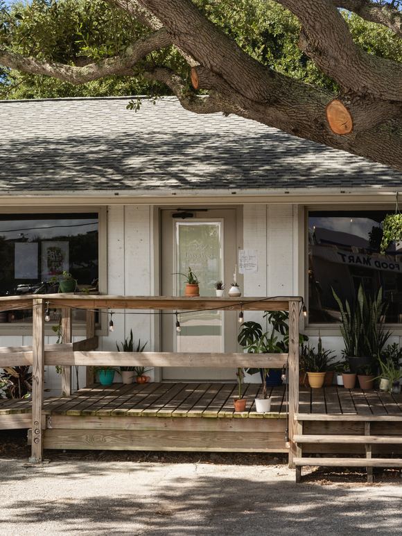 The Lines & Vines Coffee storefront on E 3rd Avenue, a white building under a live oak with potted plants along its wooden deck