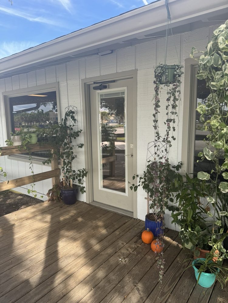 The Lines & Vines Coffee storefront on E 3rd Avenue, white building framed by hanging plants and a sunny wooden deck